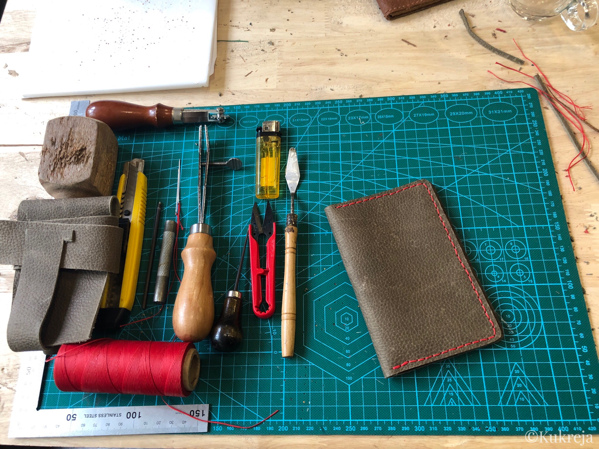 Tools for leather craft displayed on the worktable along with the finished leather passport holder. 